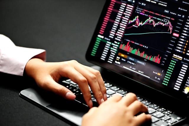 Primer plano de unas manos escribiendo junto a gráficos del mercado en tiempo real